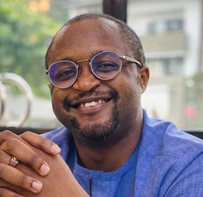 Gilead Ogbonna smiling, hands clasped, in a blue shirt